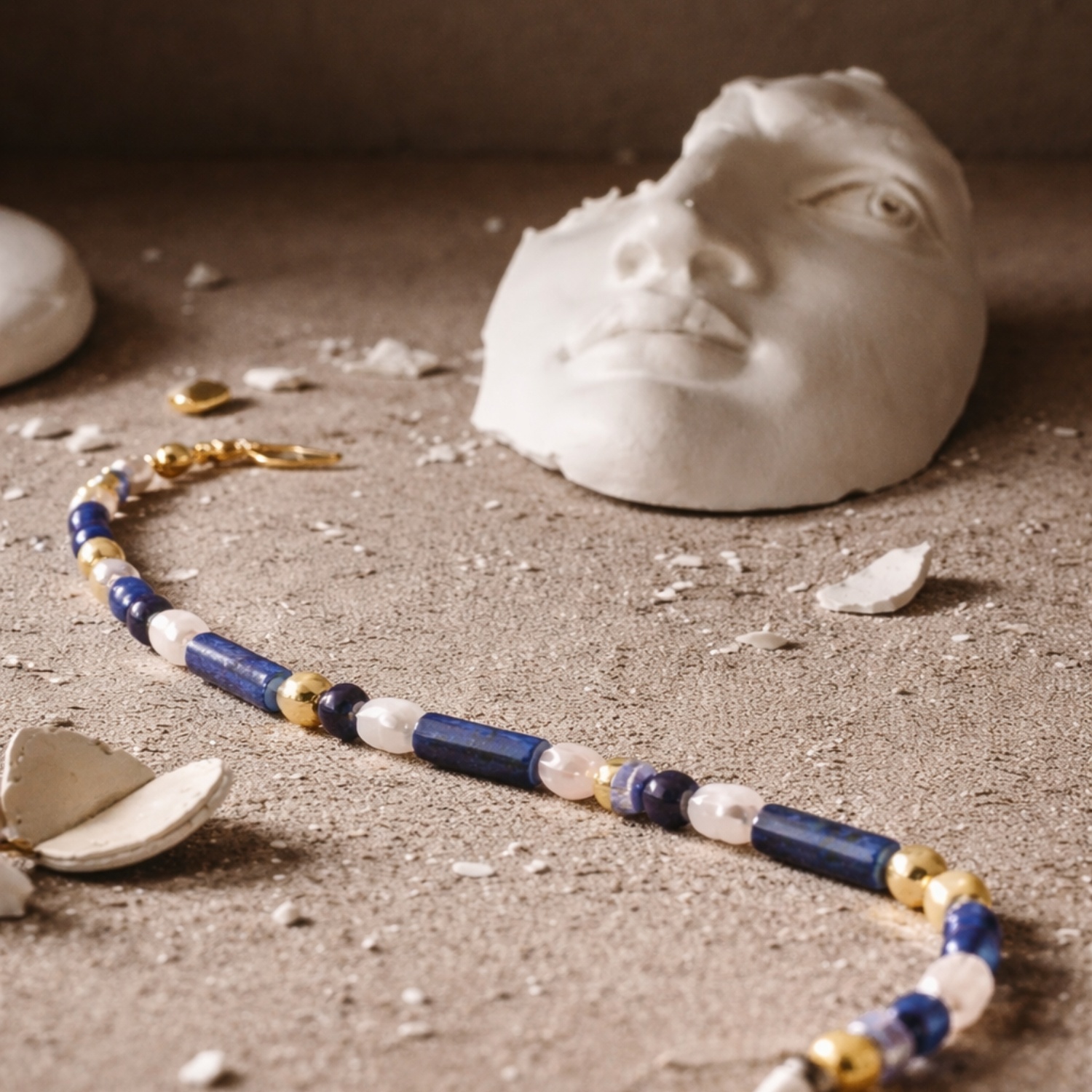 Athens Bracelet estirat sobre una superfície texturitzada amb fragments de guix i una escultura clàssica, polsera de pedres blaves, blanques i detalls daurats.