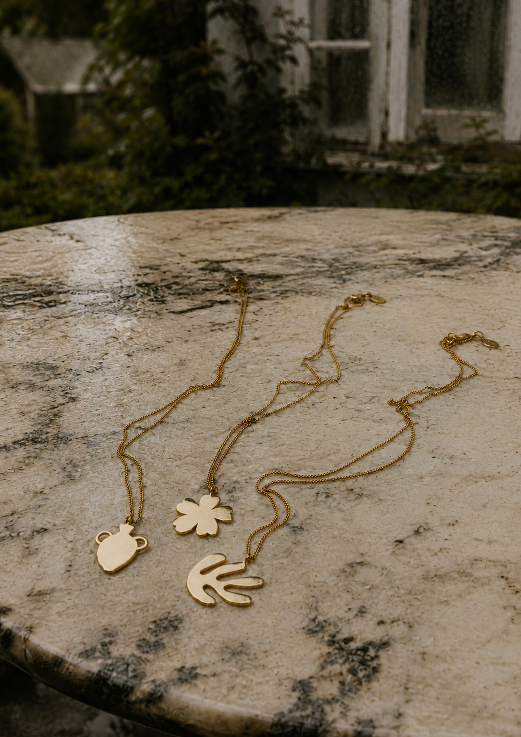 Gold flower, vase and leaf pendant necklaces on a marble table, handmade in Barcelona